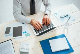 Professional businessman working at office desk and typing on a laptop, unrecognizable person